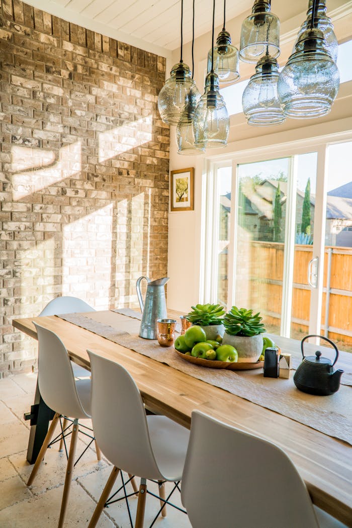 portfolio-08 Sunlit dining room with contemporary decor and a rustic brick wall, featuring stylish lighting and a wooden table.